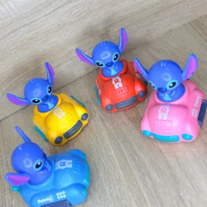 Cuatro carros de juguete de Stitch a fricción en colores azul, amarillo, rojo y rosa sobre piso de madera.